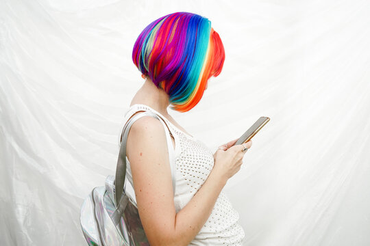 Woman with multi colored hair using smart phone by plastic backdrop