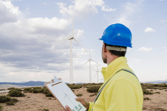 Engineer with document looking at wind turbines at wind farm