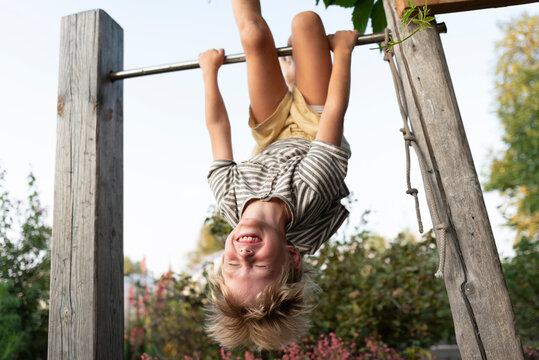Cheerful boy hanging upside down on horizontal bar