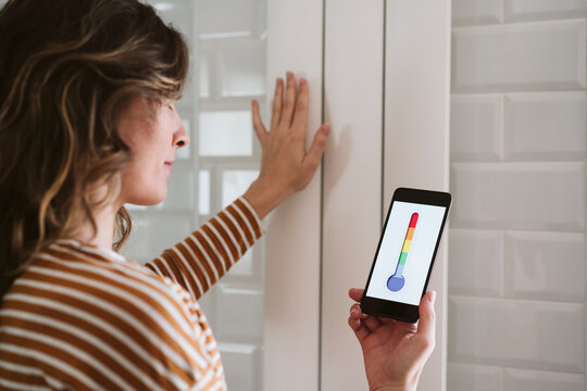 Young woman using smart phone app and touching radiator at home