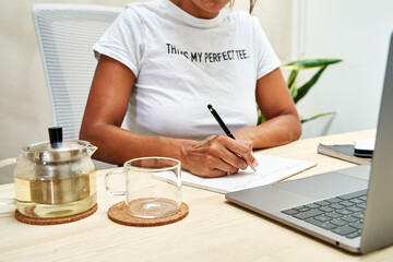 Freelancer writing on note pad working at home office