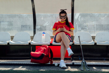 Young lacrosse player using mobile phone on bench at dugout