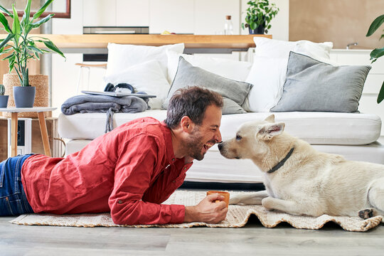 Happy man with coffee cup lying with dog at home