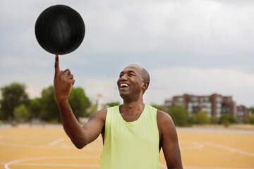 Smiling man spinning ball on finger standing at basketball court