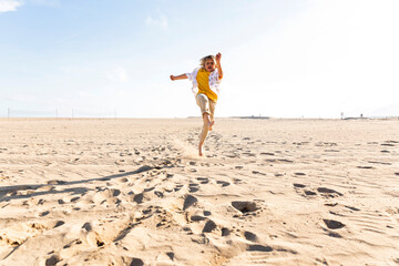 Boy jumping and playing at beach on sunny day