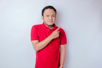 Portrait of a thoughtful young casual man wearing a red shirt pointing upside isolated over white background