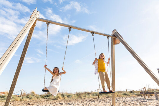 Cheerful girl with brother playing on swing at beach