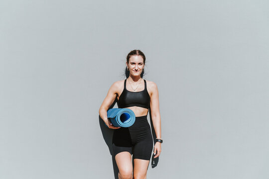 Smiling Beautiful Young Woman With Exercise Mat Leaning On Wall