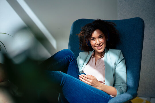 Smiling Businesswoman With Smart Phone Sitting On Chair At Office