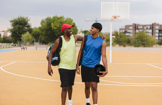 Smiling young man holding basketball walking with father at sports court