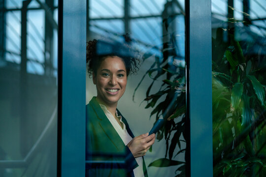 Happy businesswoman with smart phone seen through glass window
