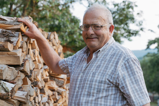 Smiling senior man by stack of firewood
