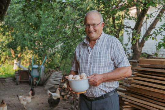 Smiling farmer holding bowl of eggs standing at farm