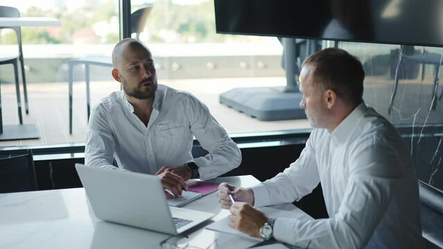 Two diverse business men discussing financial market data using laptop and digital tablet. Financial advisor broker manager consulting investor client about digital investment at office meeting