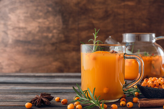 Glass and teapot with hot autumn drink. Sea buckthorn tea with orange, cinnamon and rosemary on wooden table