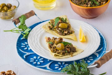 An appetizer, a salad of baked eggplant, onions, herbs and spices on tortillas on a white plate on a light concrete background. Recipes for eggplant.