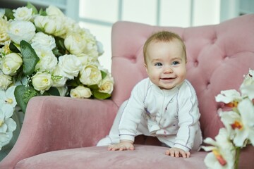 A little baby girl is sitting on a pink armchair. The concept of motherhood and childhood.