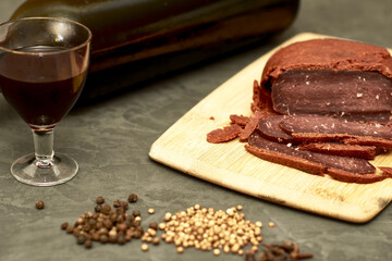 sliced basturma on a plate next to a bottle of wine and a glass