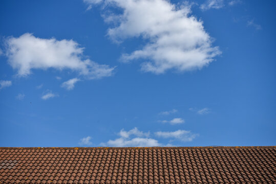 Abstract image of a brick tiled roof top contrasting with a bright blue sky with white clouds.