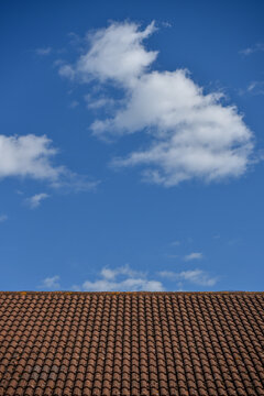 Abstract image of a brick tiled roof top contrasting with a bright blue sky with white clouds.