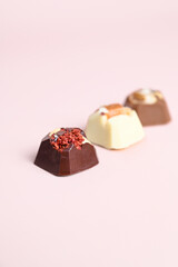 Artisan handcrafted chocolate bonbons with fruit and nuts filling. Mixed chocolate candies on pink surface. Vertical