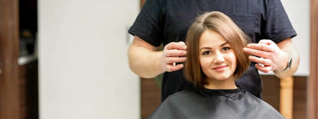 Gorgeous brunette short hair woman and her male hairdresser looking and checking out hairstyle. Beautiful hairstyle of a young brunette woman, results of hair treatment in a beauty salon