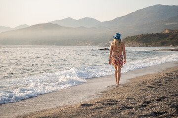 young woman walking into the sunset on a beach on the Greek island of Crete. Summer vacation in Crete
