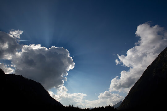Wolken am Himmel mit Sonnenstrahlen und Silhouette einer Landschaft mit Bergen