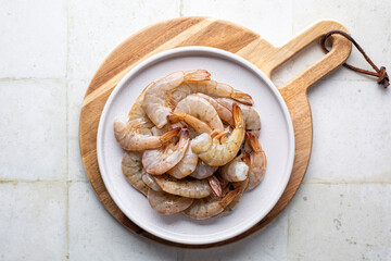 Raw fresh headless shrimp tails or prawns directly above, uncooked jumbo seafood on a white plate,...