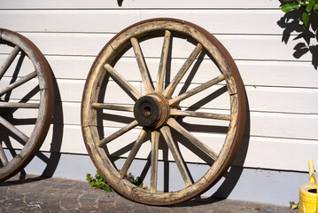 Obraz premium Wooden wheels of carriage leaned against wall of house on a sunny summer day at rural village Andelfingen, Canton Zürich. Photo taken July 12th, 2022, Andelfingen, Switzerland.