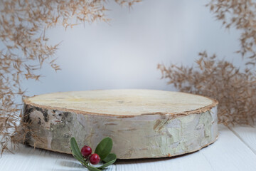 Cylindrical wooden podium on a white background with pampas grass and a sprig of cranberries. A...