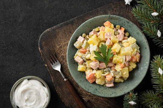 Russian Christmas or New Year salad Olivier from boiled vegetables and sausage with mayo on black table with fir tree
