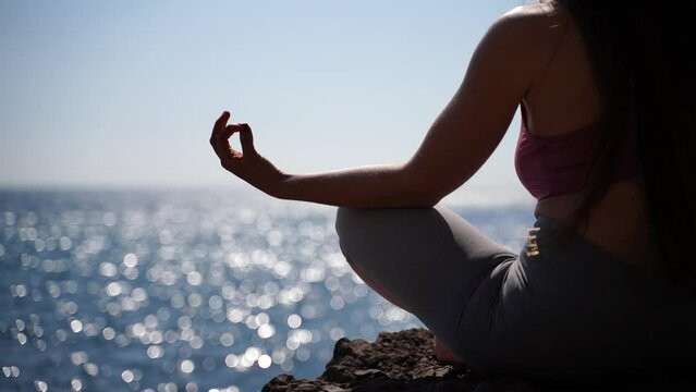 Rear view of a young beautiful caucasian woman practicing yoga on the beach at the seaside. Yoga. Healthy lifestyle. Meditation concept.