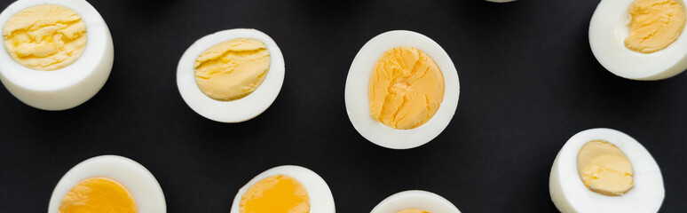 Top view of cut boiled eggs with yolks on black background, banner.