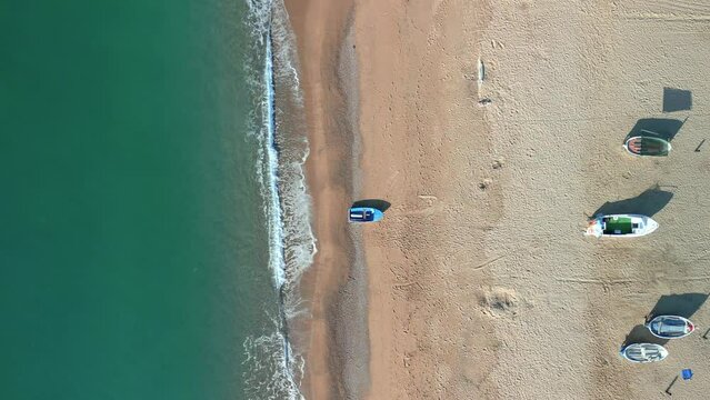 Aerial overhead view of a beach with calm turquoise blue waters, fishermen boats in the foreground