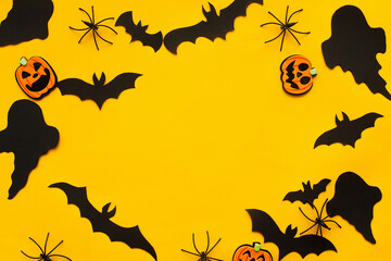 Halloween flat lay. Bats, spiders, ghost and pumpkins decoration on yellow. Happy Halloween template