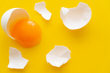 Top view of white egg shell near raw yolk on yellow background.