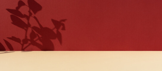 Premium podium with a shadow of plant leaves on a red wall and a beige table. Minimal abstract background for the presentation of a cosmetic product. Showcase, display case.