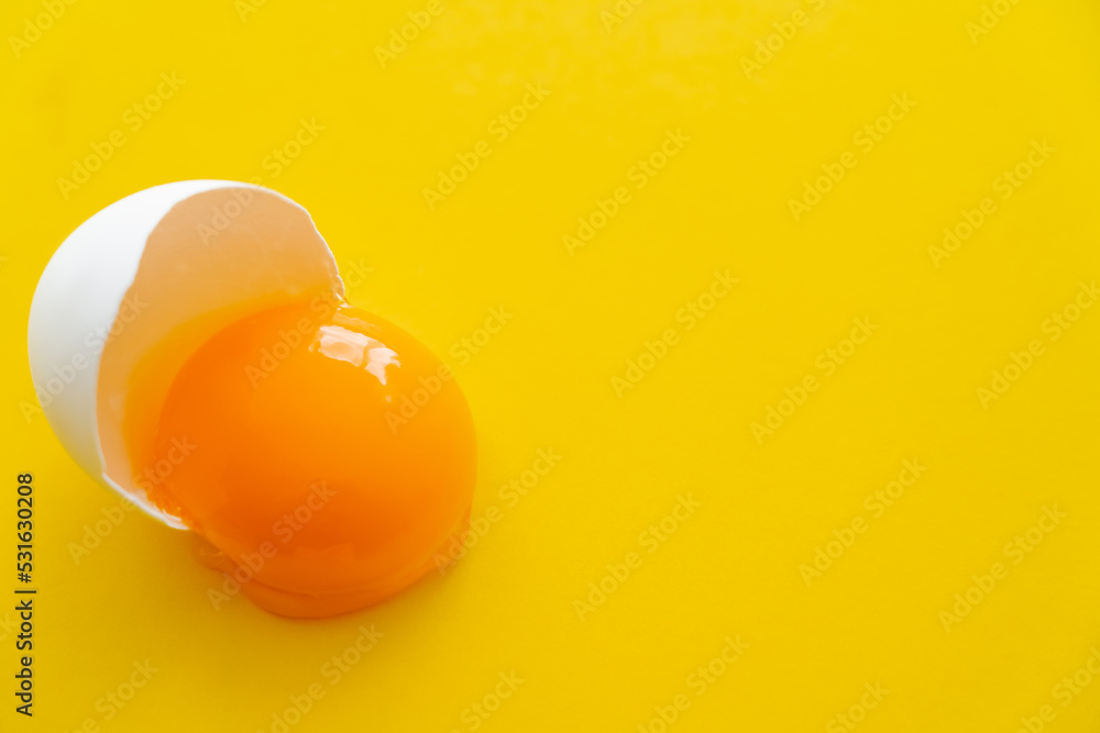 Wall mural close up view of raw natural egg yolk in shell on yellow background.