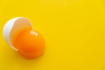 Close up view of raw natural egg yolk in shell on yellow background.