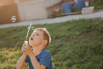 A boy is blowing bubbles in the backyard.
