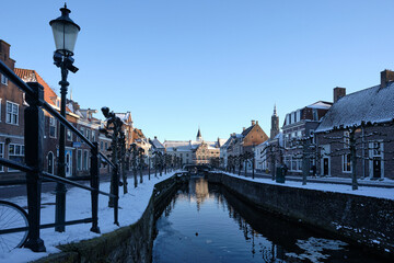 Blue hour winter scene with snow and ice in the canal in old city center of Amersfoort, Netherlands. Overlooking the streets Grote Spui and Kleine Spui with museum Flehite in the background