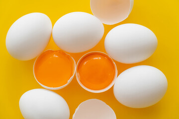 Top view of organic yolks in shells and white eggs on yellow background.