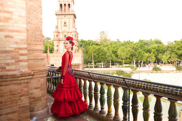 Beautiful teenage woman dancing flamenco on the balcony of a square in Seville. She wears a red...