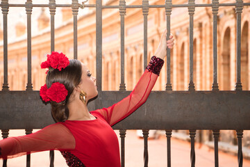 Beautiful teenage woman dancing flamenco in a square in Seville, Spain. She wears a red dress with...