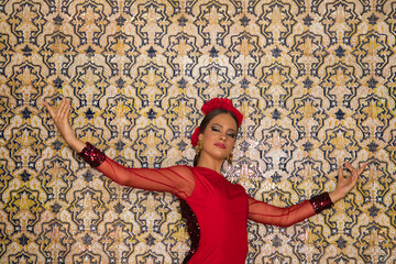 Beautiful teenage woman dancing flamenco doing different flamenco dance postures on a background of typical arabic tiles. She wears a red dress with a frill. Flamenco cultural heritage of humanity.
