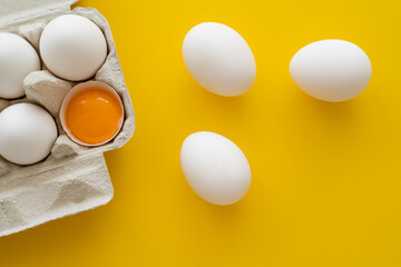 Top view of eggs and yolk in shell in package on yellow background.