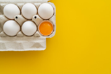 Top view of yolk in shell near eggs in cardboard box on yellow background.