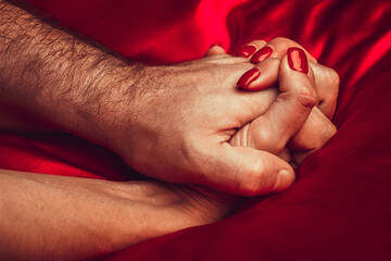 Close up of man and woman hands who lie on the bed. Passionate holding each other hand during while...