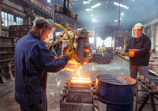 Workers pouring molten metal into mold in iron foundry